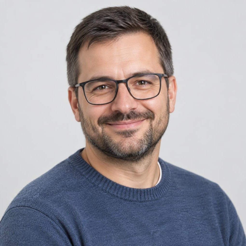 Studio portrait of a smiling man with glasses in a casual sweater